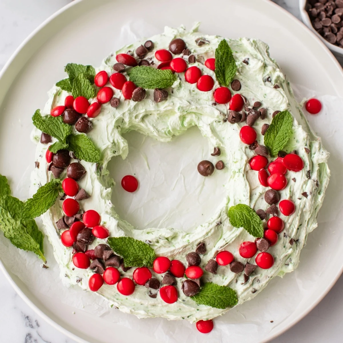 Festive Mint Chocolate Chip Dip Wreath, a creamy dessert decorated with red candies and fresh mint.