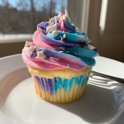 A vibrant Magical Unicorn Dessert Table overflowing with colorful cupcakes, kisses, and cookies.