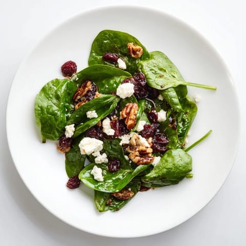 Ein heller, appetitanregender Spinat Ziegenkäse Salat mit goldbraunen Pekannüssen und süßen Cranberries auf rustikalem Holzteller angerichtet.
