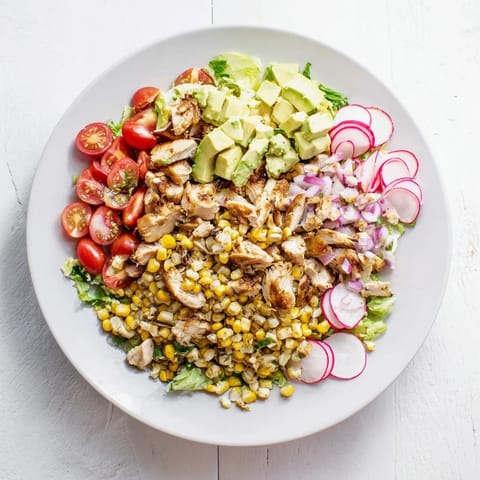 Eine frische Schüssel Roasted Corn & Chicken Chopped Salad mit gegrilltem Mais und saftigem Hähnchen auf Rucola mit Avocado-Scheiben und einem zitronigen Dressing.