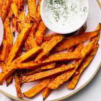 Crispy oven-baked sweet potato fries, served hot alongside the creamy herbed yogurt dip.