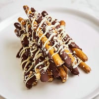 A stack of chocolate-covered pretzel sticks with white chocolate drizzle, ready to eat.